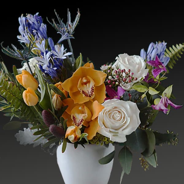 Mixed bouquet in a white vase with white roses, orange orchids, and blue flowers