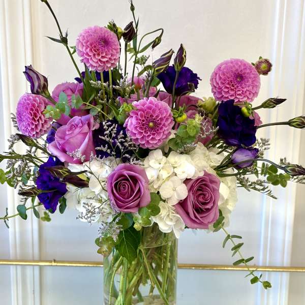 Pink and purple bouquet with roses, dahlias, and white hydrangeas in a glass vase