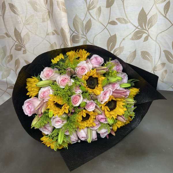 Bouquet of pink roses, sunflowers, and lilies wrapped in black paper