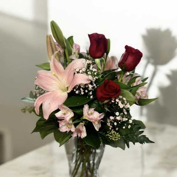 Bouquet of red roses and pink lilies in a clear glass vase