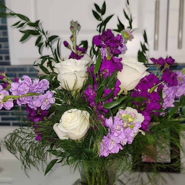 White roses and purple flowers arranged in a clear glass vase