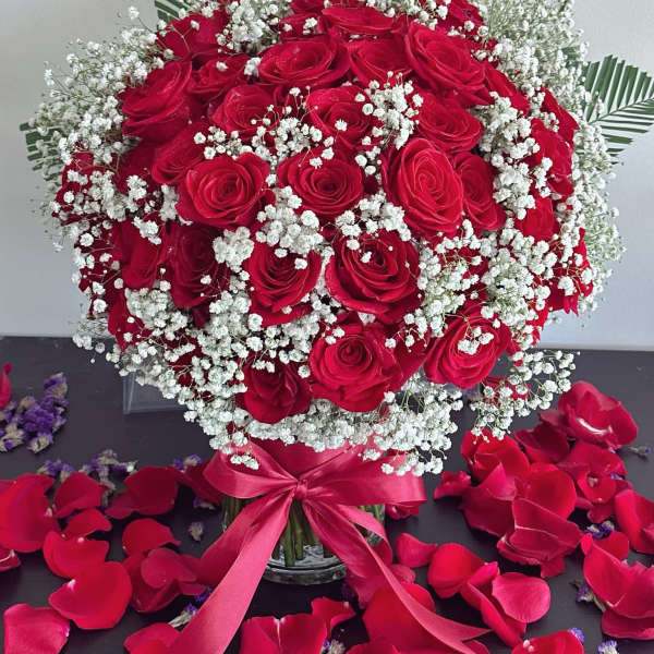 Red rose bouquet with baby's breath in a glass vase and ribbon