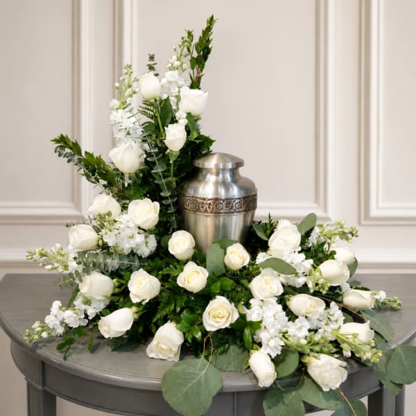 White roses and stock arranged around a silver urn on a table
