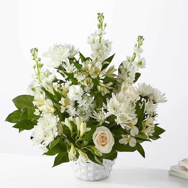 White floral arrangement in a white basket with a pale rose accent