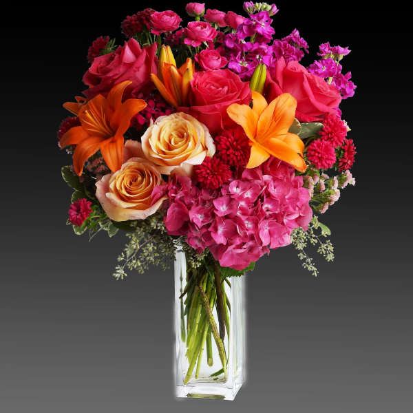 Bright mixed bouquet of roses, lilies, and pink blooms in a clear glass vase.