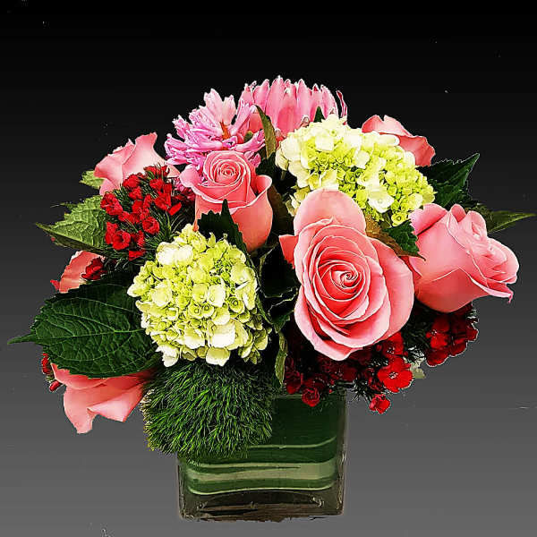 Pink roses and mixed blooms arranged in a square glass vase