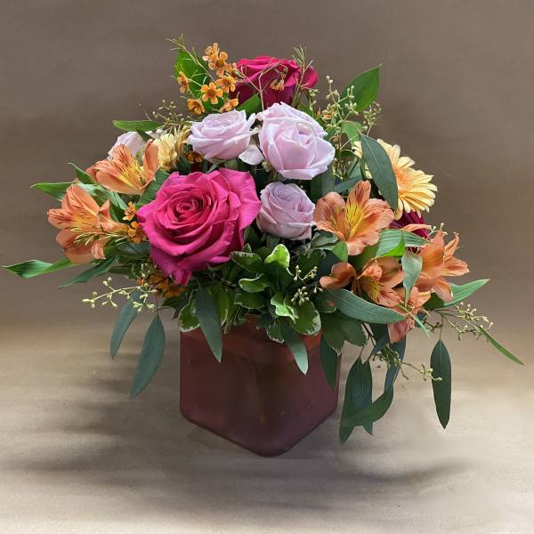 Mixed bouquet of pink roses and orange alstroemeria in a burgundy vase