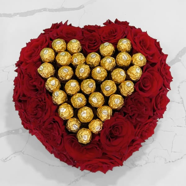 Heart-shaped red rose arrangement with gold-wrapped chocolates in the center