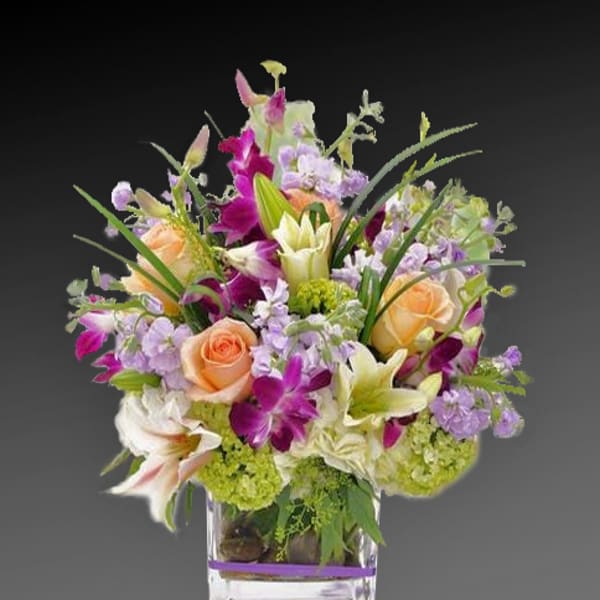 Mixed bouquet of roses, lilies, and purple flowers in a clear glass vase