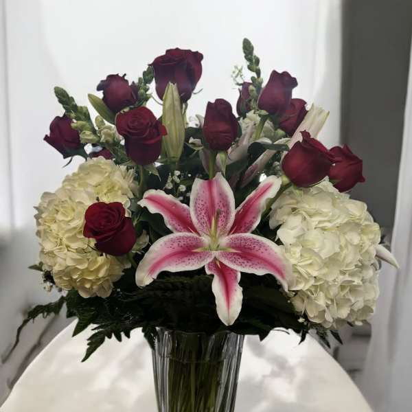Bouquet of red roses, white hydrangeas, and a pink lily in a clear vase
