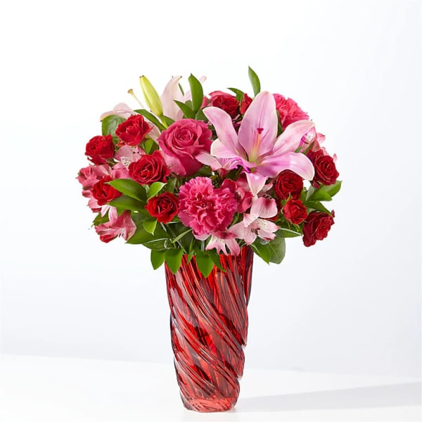 Pink lilies and red roses arranged in a red glass vase