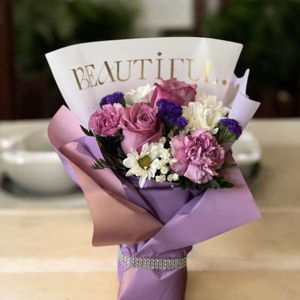 Pink and purple bouquet with roses, carnations, and daisies in decorative wrap