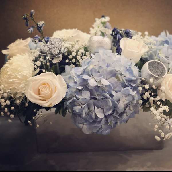 Blue hydrangeas and cream roses arranged in a low box