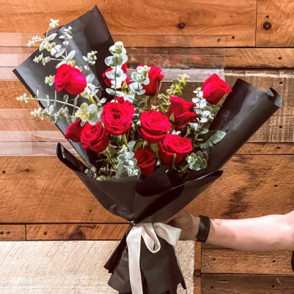 Bouquet of red roses with eucalyptus wrapped in black paper and tied with a white ribbon