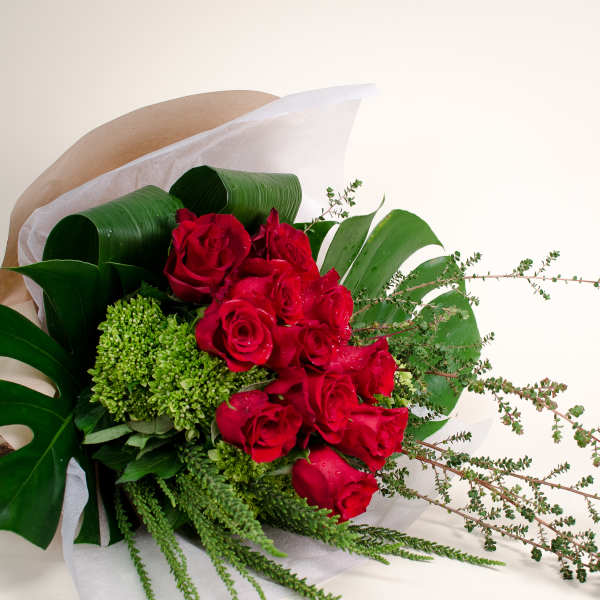 Bouquet of red roses with green filler and broad tropical leaves