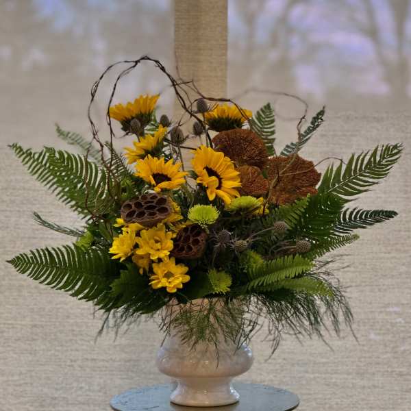 Yellow flowers arranged in a white vase with fern-like greenery