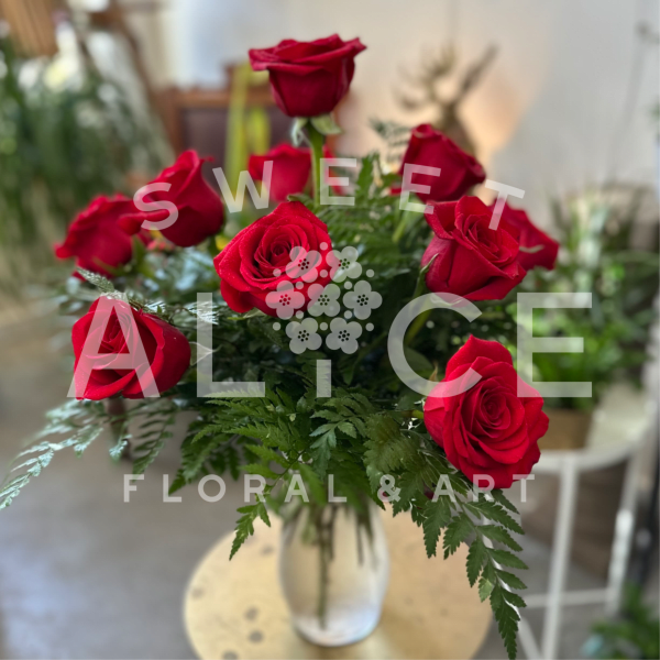 Arrangement of red roses in a clear glass vase with ferns on a small round table.