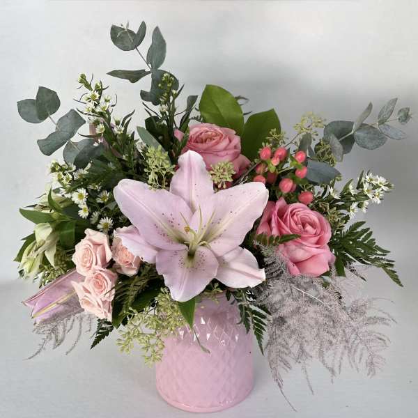 Pink roses and a pale lily arranged in a pink vase