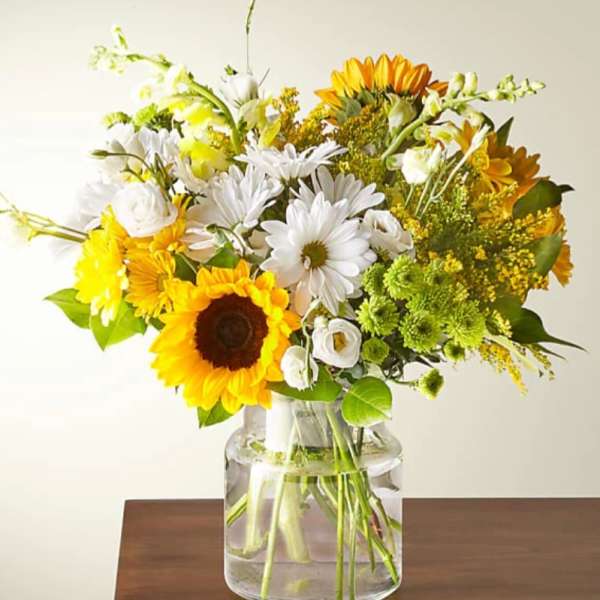 Bouquet of sunflowers, white daisies, and yellow flowers in a glass vase