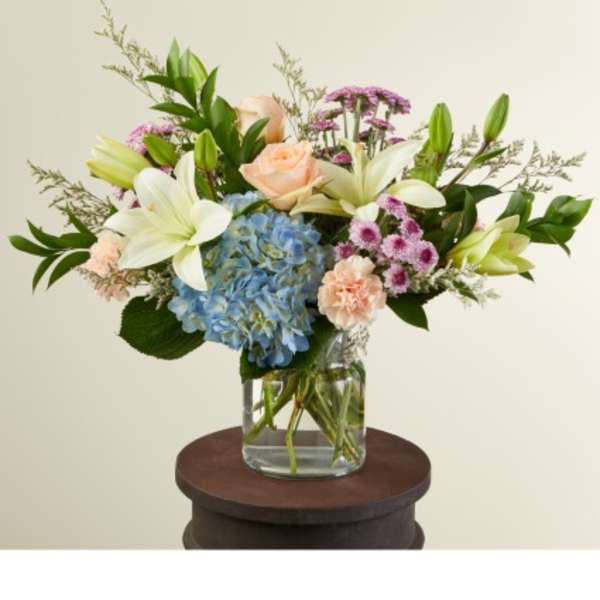 Mixed bouquet in a clear glass vase with blue hydrangea, white lilies, and peach roses