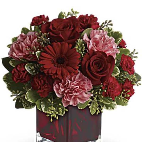 Red and pink flower arrangement in a square glass vase