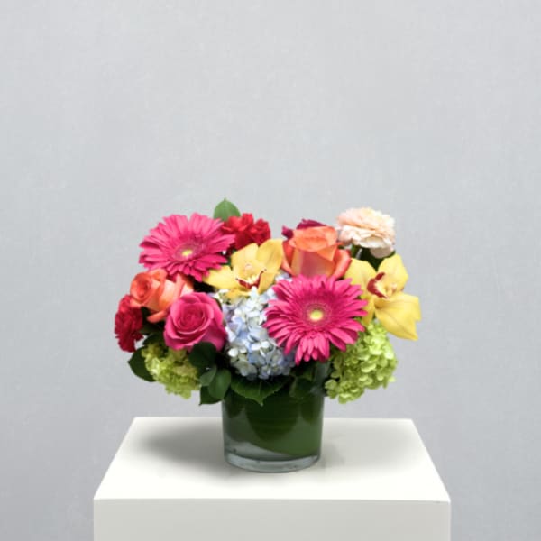 Mixed bouquet in a green glass vase with pink, yellow, and orange flowers