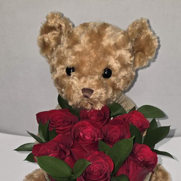 Teddy bear holding a bouquet of red roses with a heart ribbon