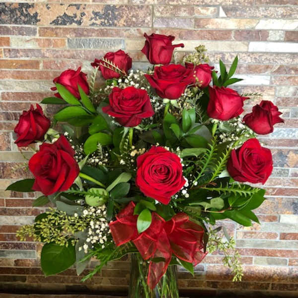 Red roses arranged in a clear glass vase with a red ribbon