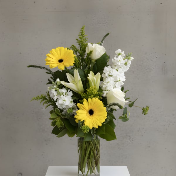 Yellow gerbera daisies and white lilies in a clear glass vase
