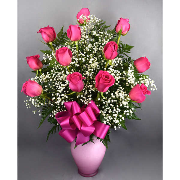 Pink roses in a pink vase with baby's breath and a ribbon bow