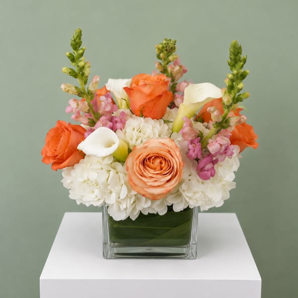 Orange roses and white calla lilies in a square glass vase