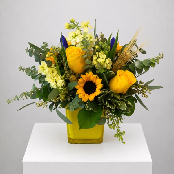 Yellow roses and a sunflower in a yellow vase with mixed greenery