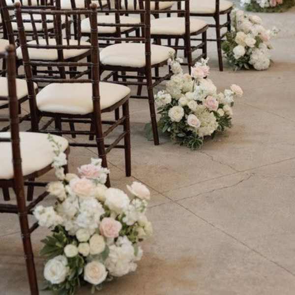 Pastel floral arrangements line rows of chairs in a ceremony space.