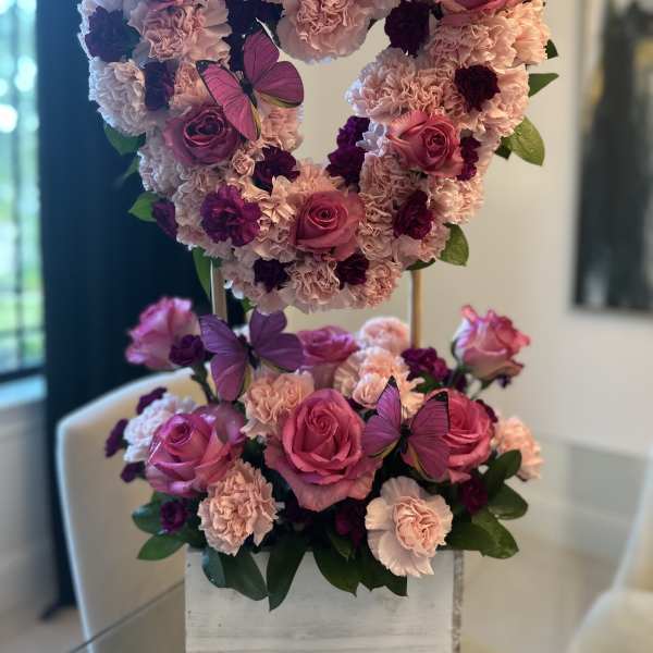 Heart-shaped floral arrangement with pink roses, carnations, and purple butterflies