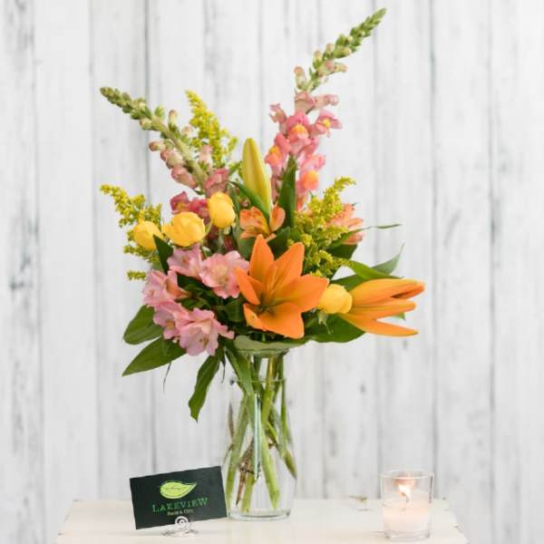 Mixed bouquet of orange lilies, pink snapdragons, and yellow tulips in a glass vase