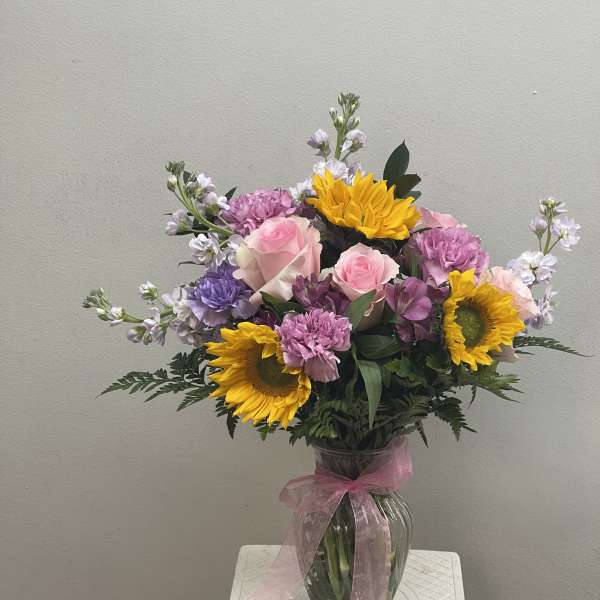 Mixed bouquet of pink roses, sunflowers, and purple blooms in a glass vase