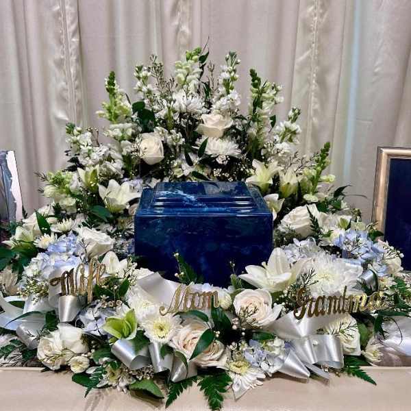 White floral funeral arrangement surrounding a blue urn with memorial name signs