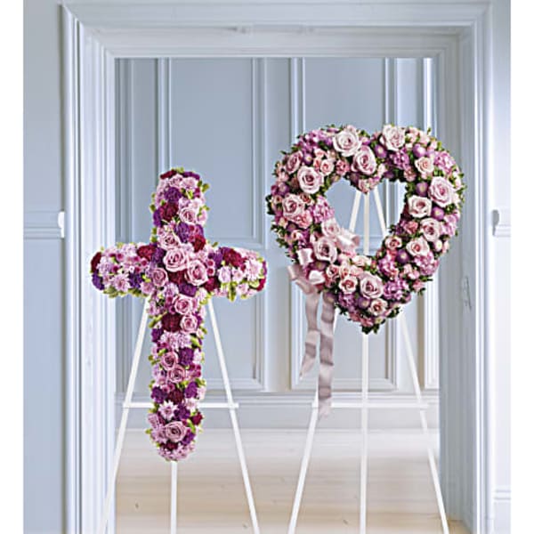 Two floral funeral tributes on white stands, one cross and one heart-shaped