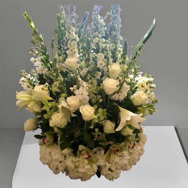 Tall white floral arrangement with roses, lilies, and blue spikes