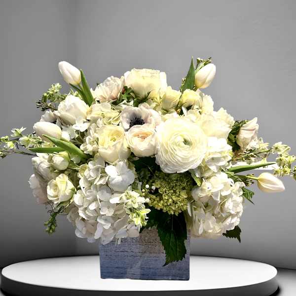 White floral arrangement in a square vase with tulips and roses