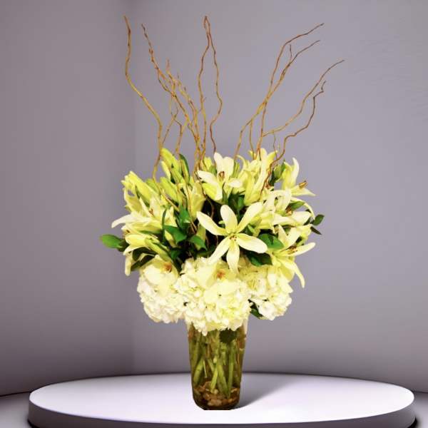 White lilies and hydrangeas in a tall glass vase with curly branches