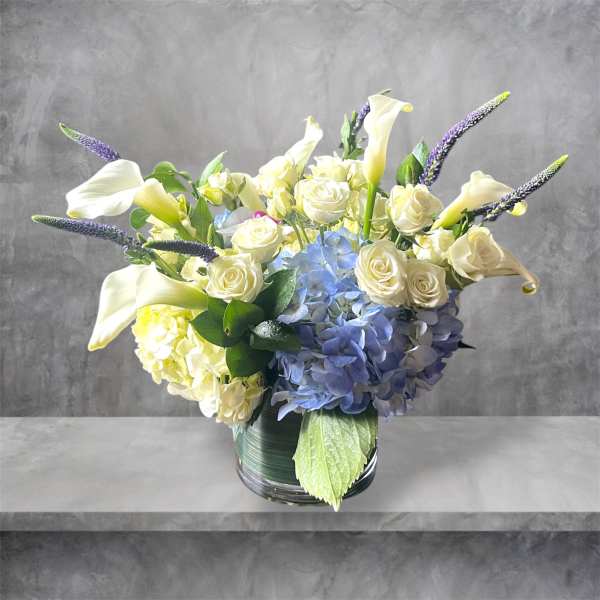 Bouquet of white roses, calla lilies, and blue hydrangeas in a glass vase
