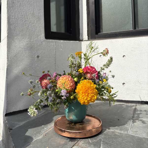 Mixed bouquet of bright orange, pink, and purple flowers in a teal vase