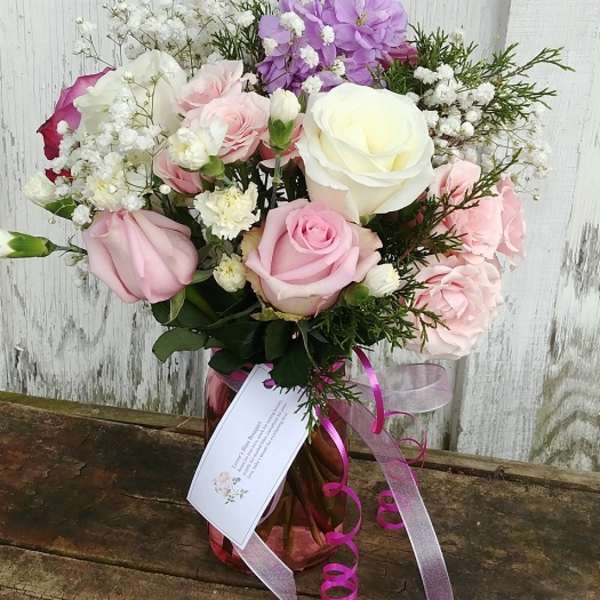 Pink and white rose bouquet in a glass vase with purple flowers