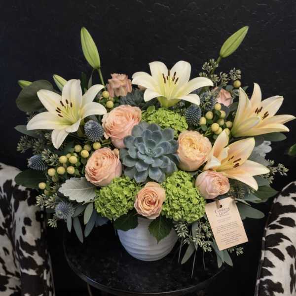 Peach roses and white lilies arranged in a white vase with a succulent centerpiece