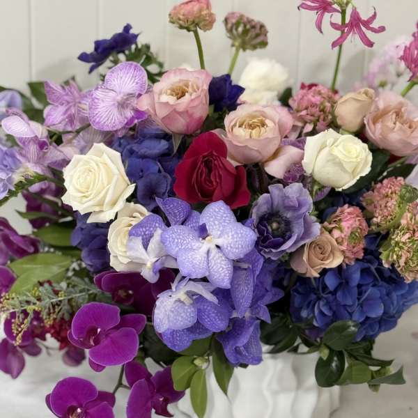 Mixed bouquet of roses, orchids, and hydrangeas in a white vase