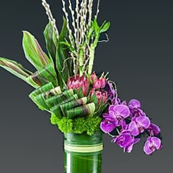Tall floral arrangement with purple orchids in a green vase