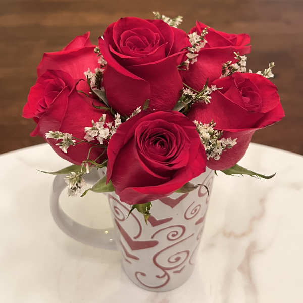 Red roses arranged in a white mug with heart designs