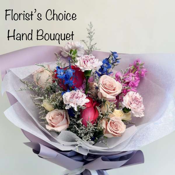 Hand bouquet of pink roses, carnations, and blue flowers wrapped in lavender paper