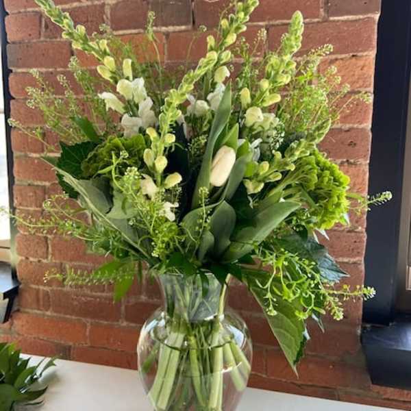 Green and white floral arrangement in a clear glass vase